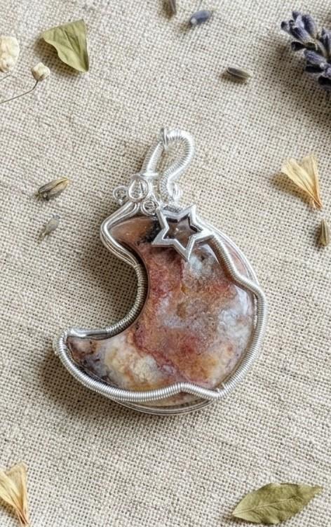 Handgemaakte verzilverde wire-wrap hanger van Bloemagaat in de vorm van een halve maan met een zilveren sterretje op een linnen achtergrond.