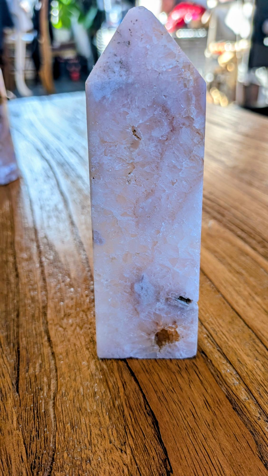 "Gepolijste kristal toren van Bloemagaat met zichtbare witte kwarts-kristallen, staand op een houten tafel met warme lichtinval."