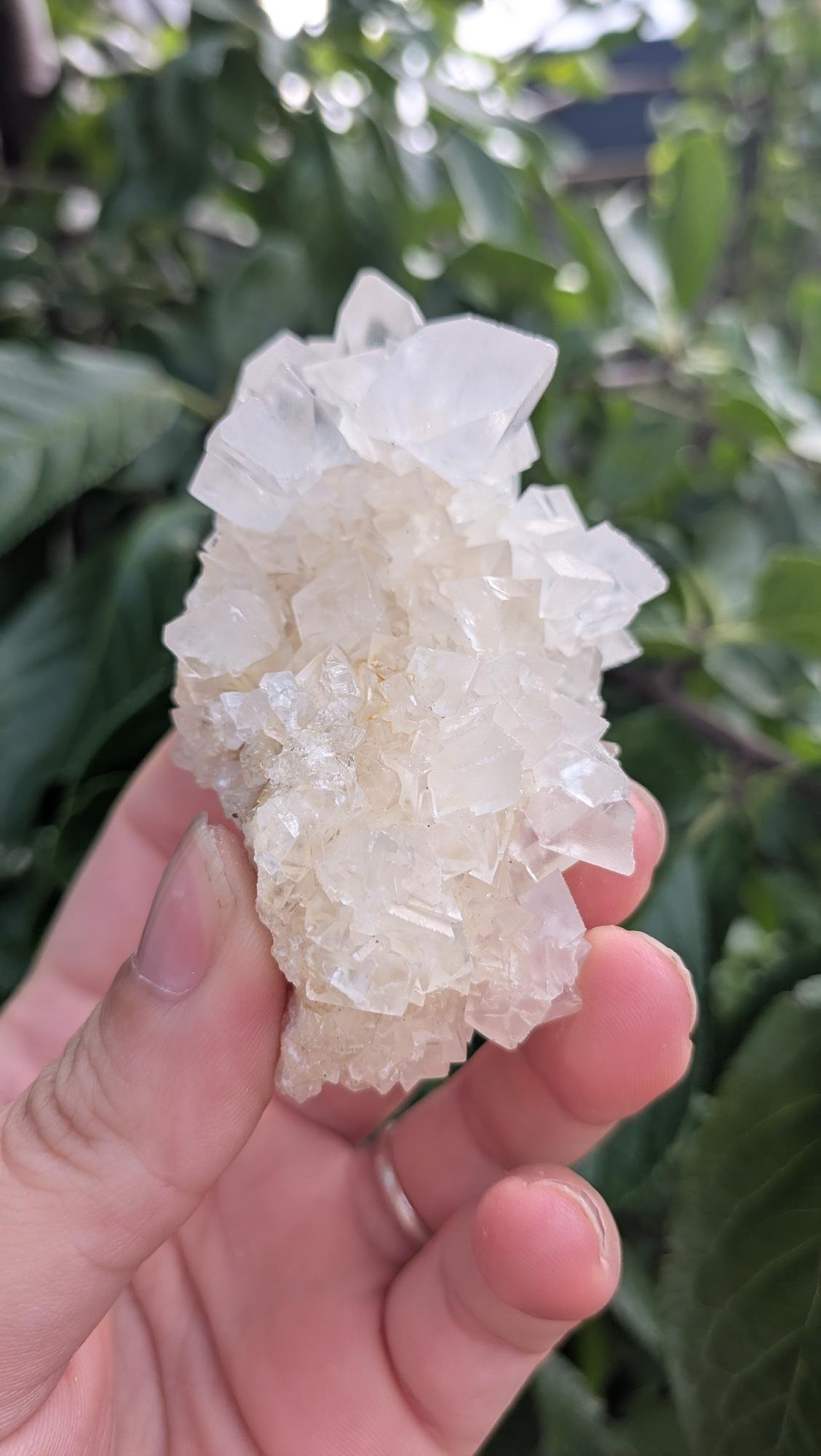 Een hand houdt een gedetailleerd en helder calciet cluster uit Indonesië van 94 gram vast, met een unieke, natuurlijke kristalstructuur