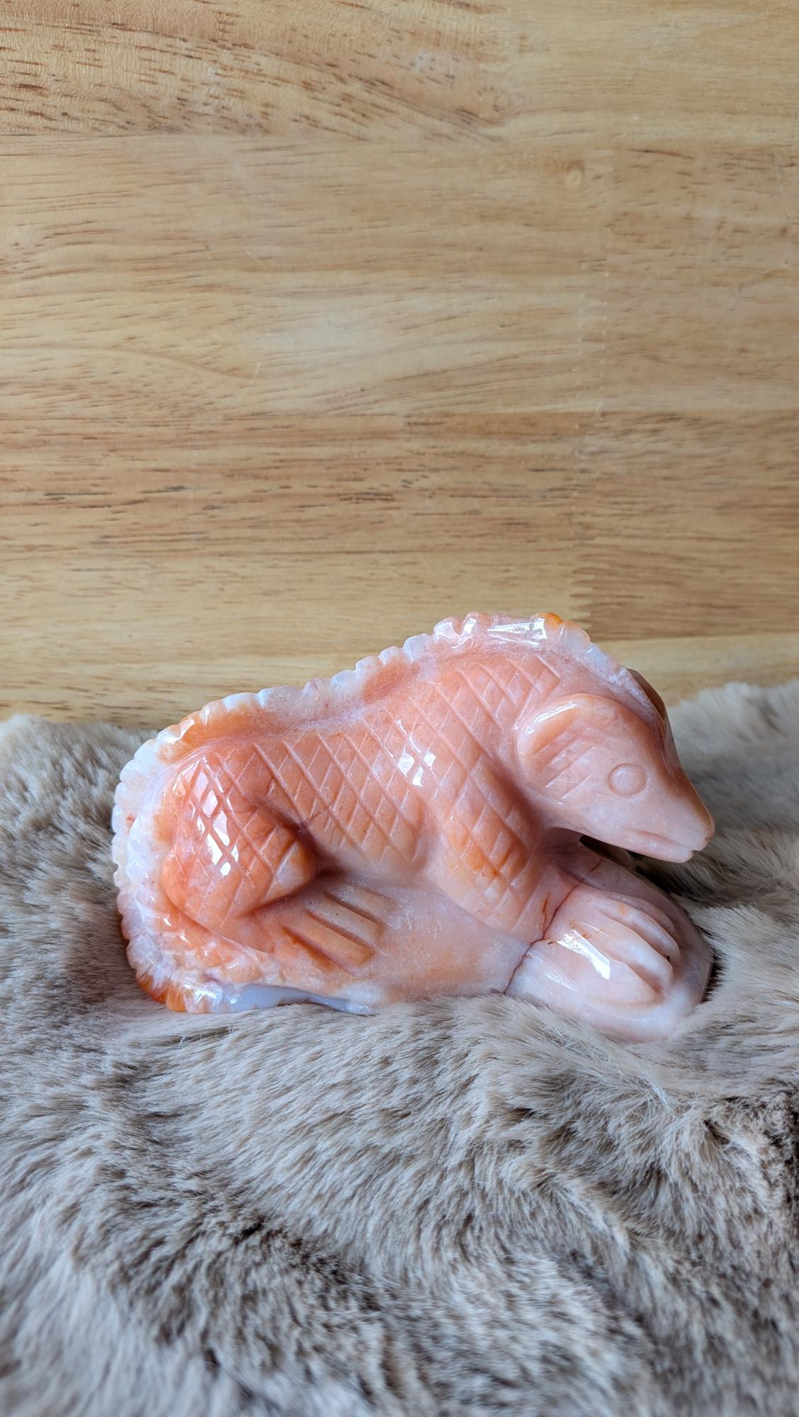Handgesneden hagedis carving van warme carneool bloemagaat met gedetailleerde schubben op een zachte achtergrond.