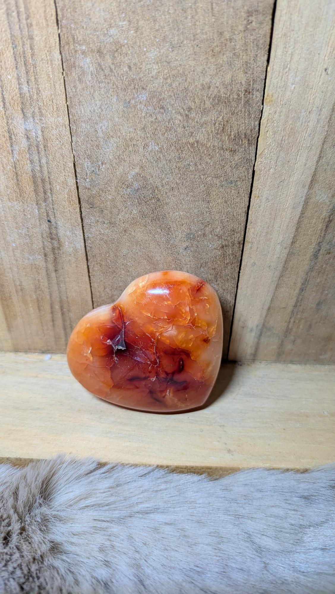 Middelmaat edelsteen hart van carneool met oranje tinten en druzy kristallen op een houten achtergrond