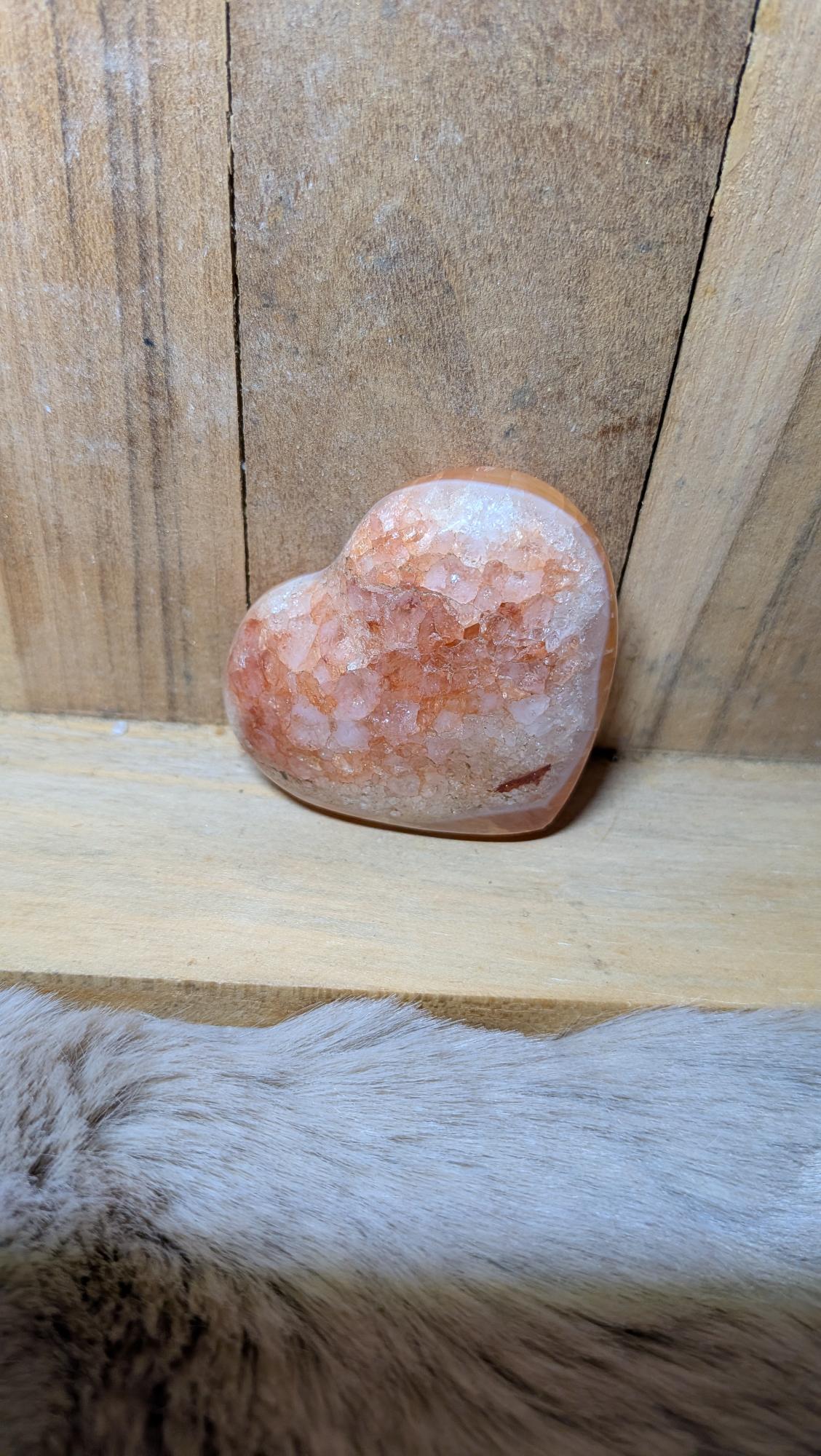 Middelmaat edelsteen hart van carneool met oranje tinten en druzy kristallen op een houten achtergrond