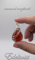 Handgemaakte wire wrapped hanger van Edeltwist met een dieporanje carneool edelsteen in een zilveren wikkeling tegen een neutrale studio achtergrond.