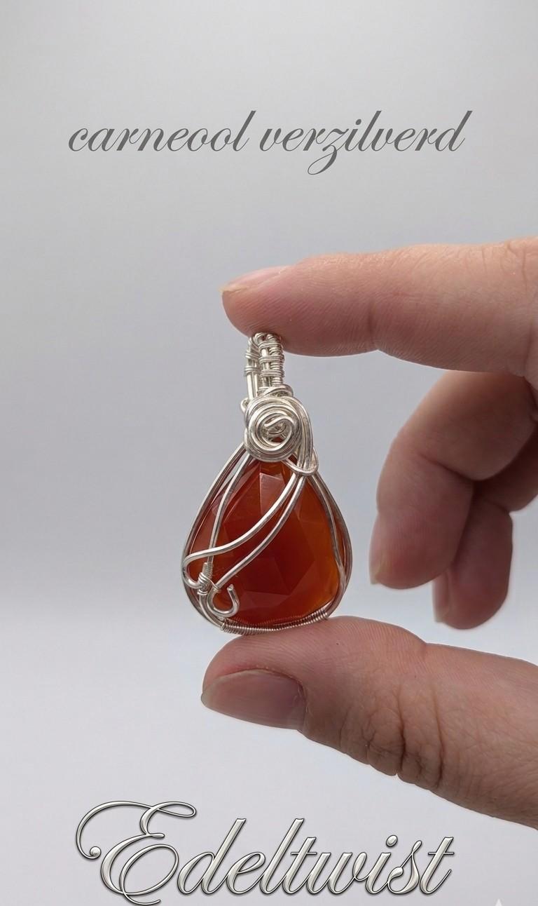 Handgemaakte wire wrapped hanger van Edeltwist met een dieporanje carneool edelsteen in een zilveren wikkeling tegen een neutrale studio achtergrond.