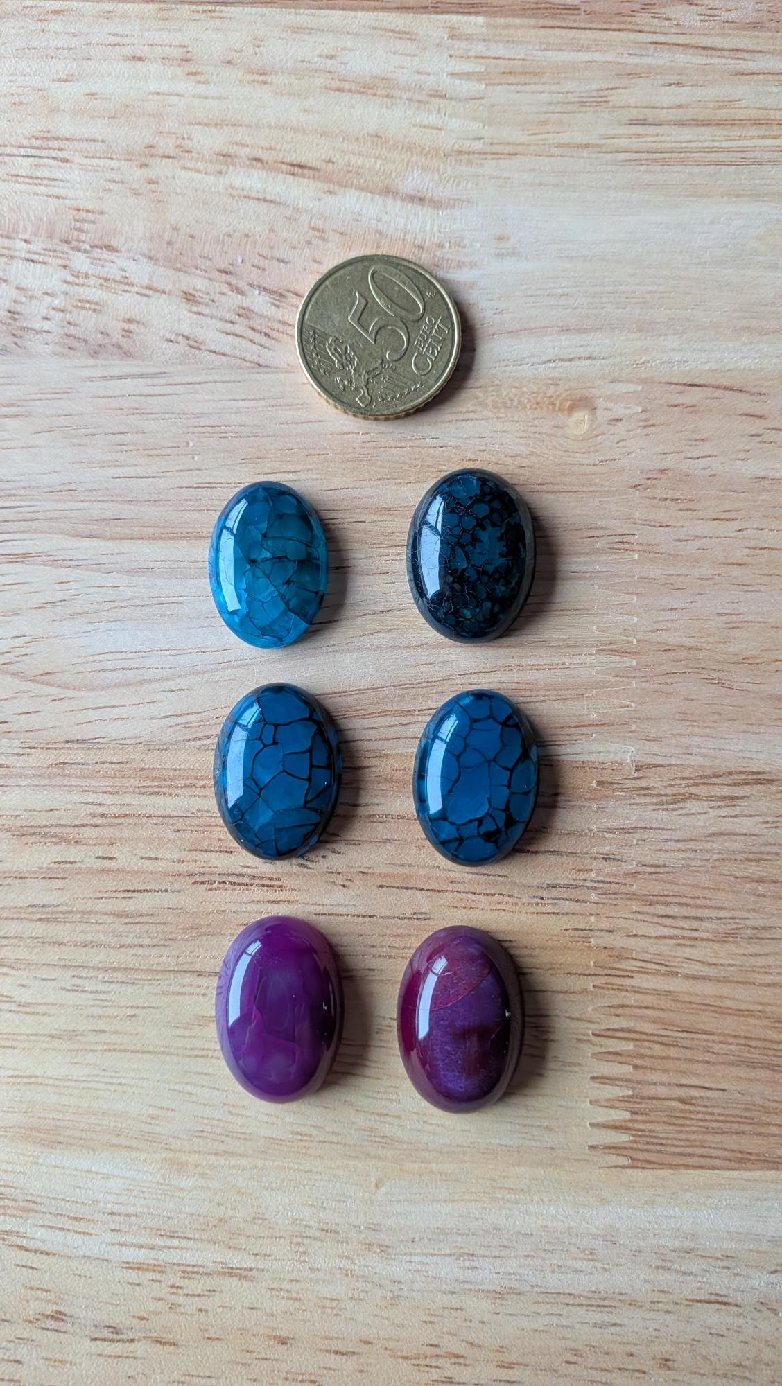 Zes ovale Drakenader Agaat cabochons in blauwe, zwarte en paarse tinten op een houten achtergrond met een 50 cent muntstuk voor de maat.