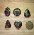 Selectie van Drakenbloed Jaspis edelstenen in hart-, ovaal-, driehoek- en cirkelvorm naast een 50 eurocent munt.