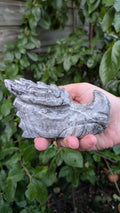 Gedetailleerde handgemaakte draken schedel van 439 gram in Picasso jaspis met grijze en zwarte patronen, vastgehouden in de hand.