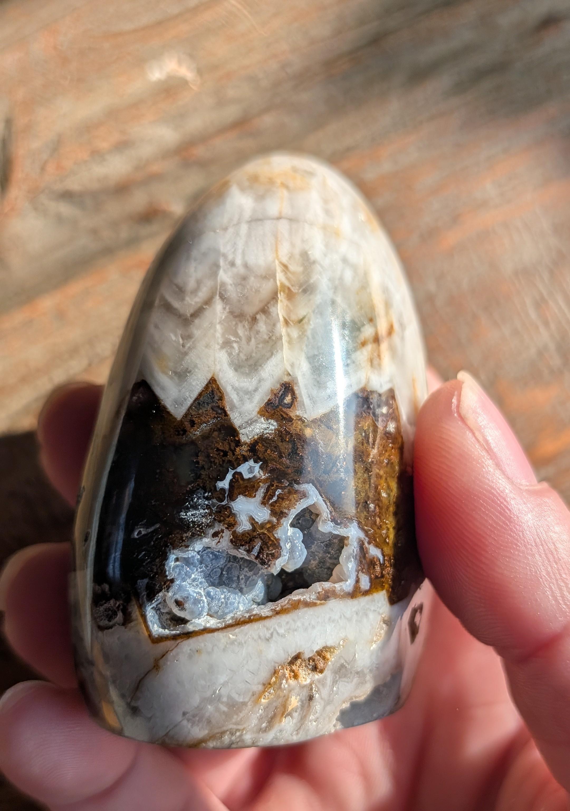 Handgepolijste Olijf Agaat freeform van 218 gram met een opvallende natuurlijke kristalholte vol fonkelende druzy, staand op een houten ondergrond.