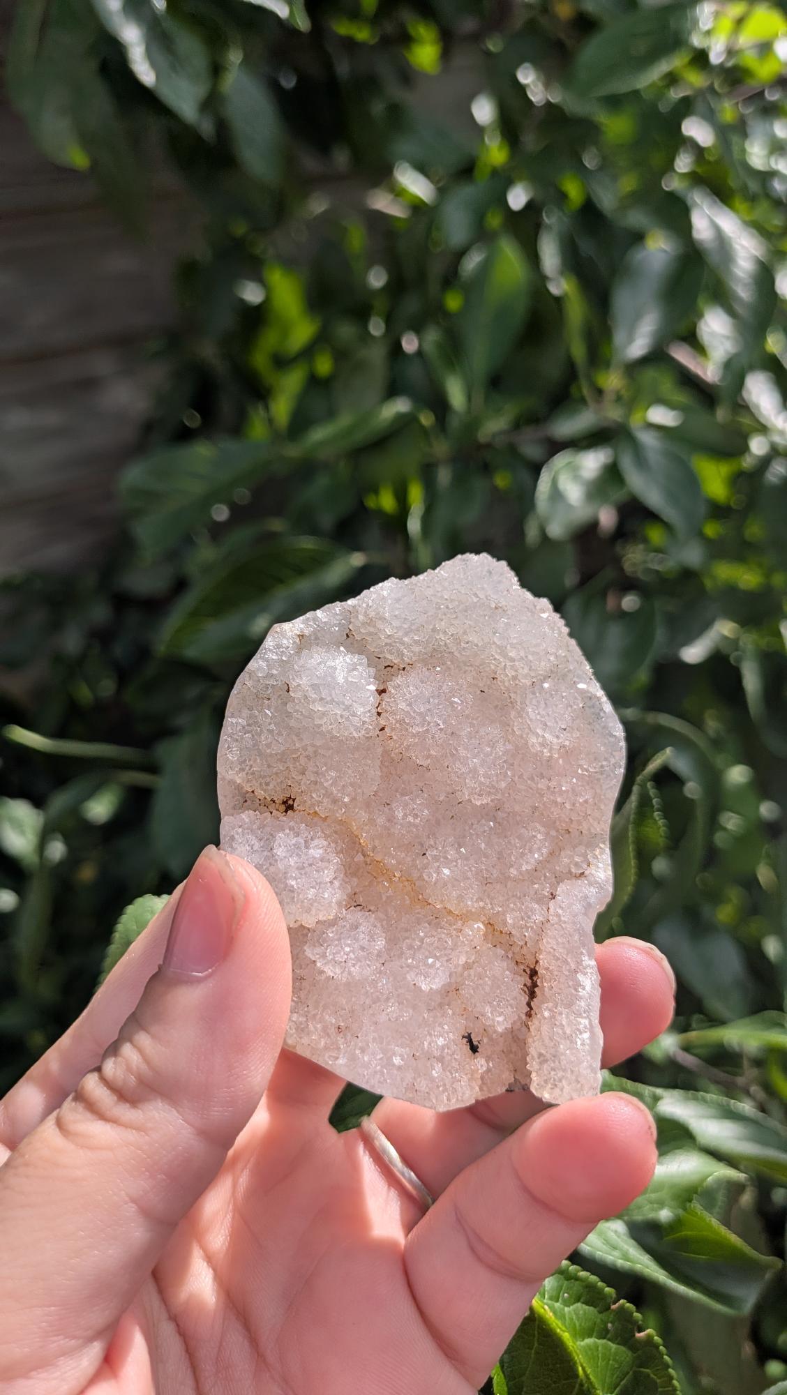 Een hand houdt een sprankelende suiker druzy chalcedoon van 49 gram vast, met een fijne, suikerachtige kristaltextuur