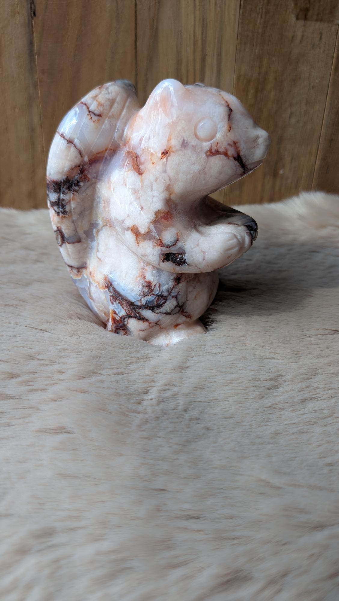 Vooraanzicht van een roze bloemagaat eekhoorn van 302 gram op een houten ondergrond.