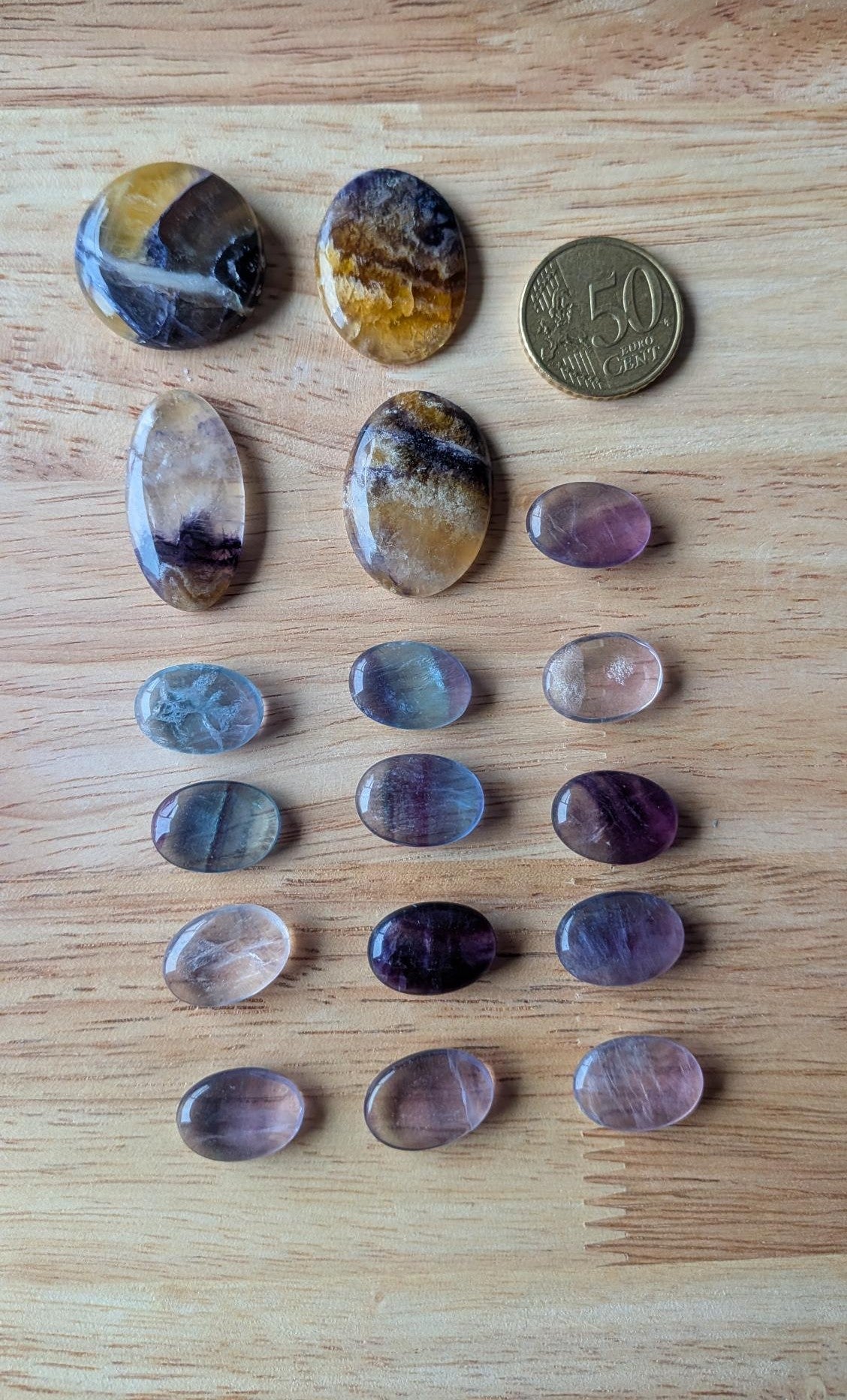 Zeventien verschillende natuurlijke fluoriet edelstenen in paarse, blauwe en gele tinten op een houten ondergrond naast een 50 cent muntstuk.