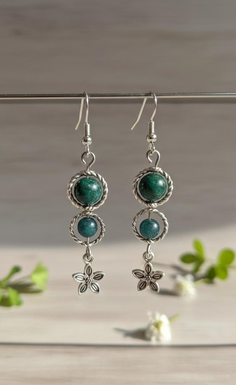 Handgemaakte zilverkleurige oorbellen met twee metalen cirkels, donkergroene ronde aventurijn kralen en een klein bloemetje onderaan.