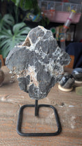 Ruwe donkergrijze agaat geode met gele druzy kwarts kristallen op een zwart metalen statief, item nummer 213.