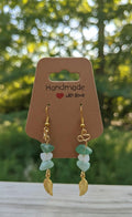 Handgemaakte goudkleurige oorbellen met een blaadje bedeltje en groene en witte edelsteen splitkralen op een "Handmade with love" kaartje.