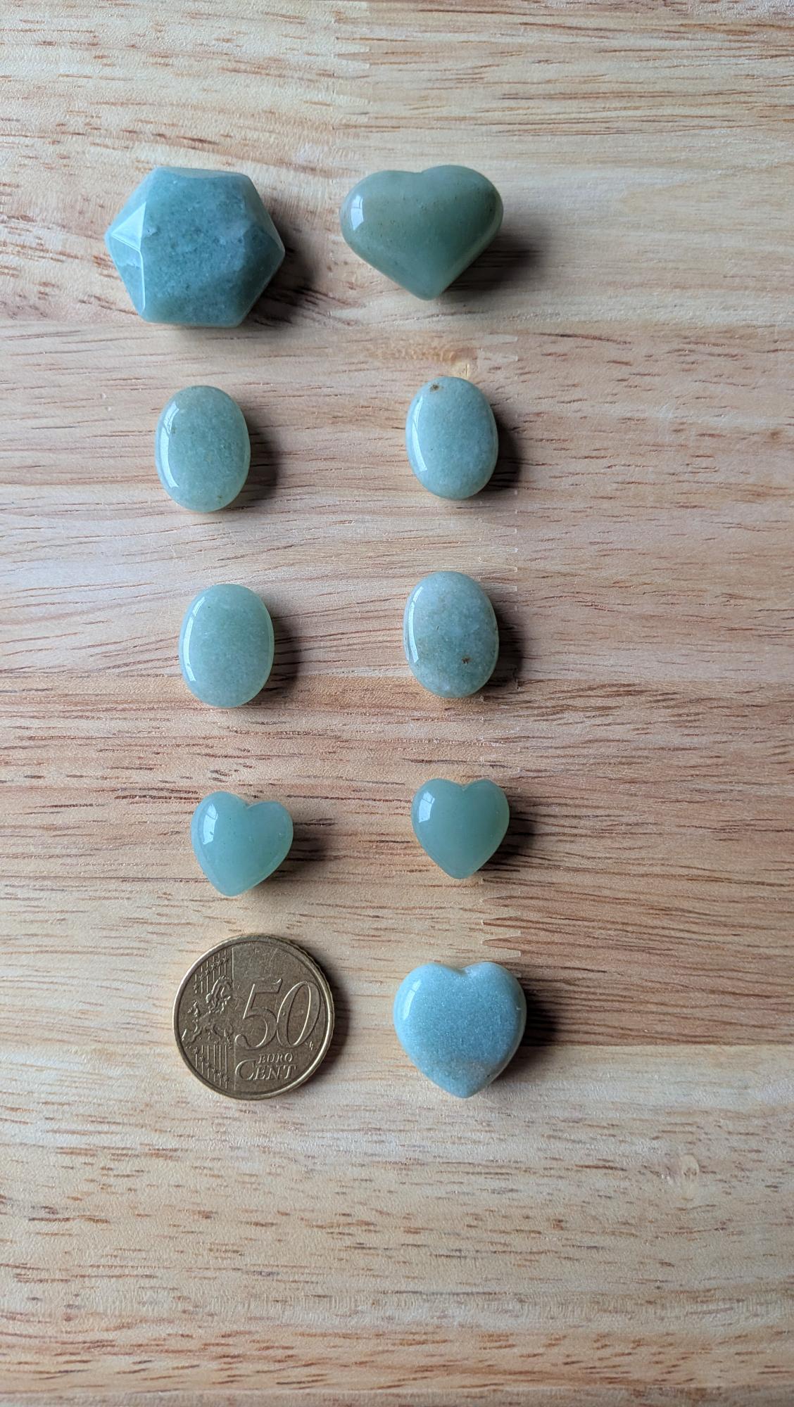 Diverse Groene Aventurijn edelstenen in hartvorm, ovaal en zeshoek op een houten ondergrond met een 50 cent muntstuk ter vergelijking.