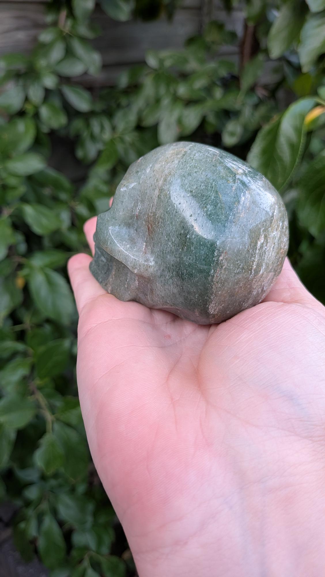 Kristallen schedel van 373 gram in groene aventurijn met subtiele glans, vastgehouden in de hand.