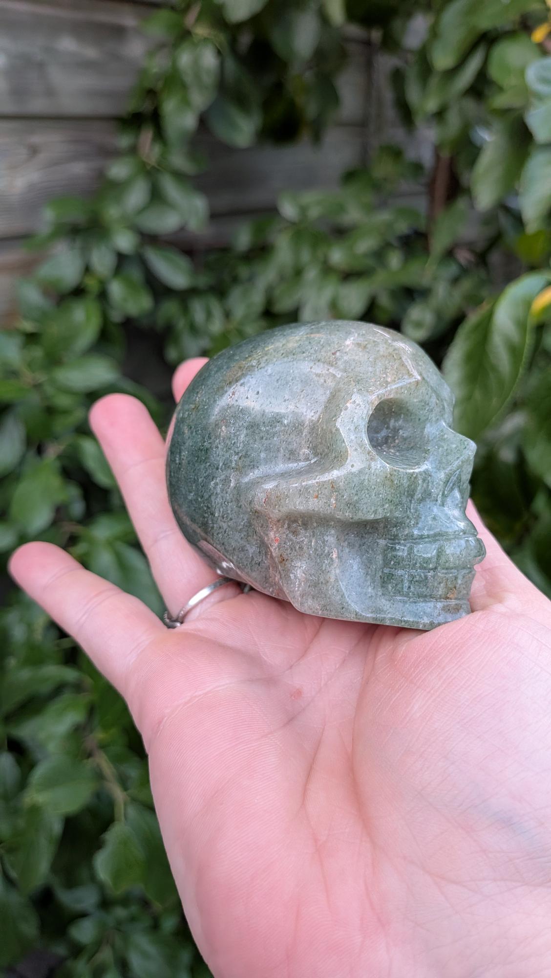 Kristallen schedel van 373 gram in groene aventurijn met subtiele glans, vastgehouden in de hand.