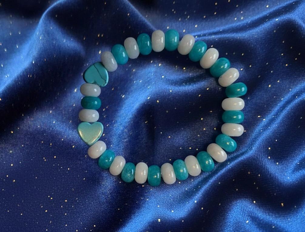 Handgemaakte edelsteen armband met ronde blauwe en witte kraaltjes en twee blauwe hartvormige edelstenen op een glanzende blauwe satijnen achtergrond
