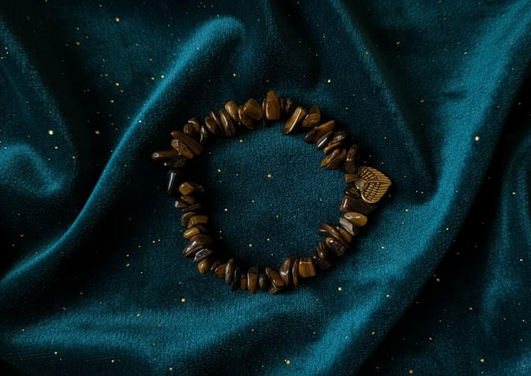 Handgemaakte natuursteen armband van goudbruine tijgeroog chips met een goudkleurige hart-bedel op een petrolblauwe fluwelen achtergrond.