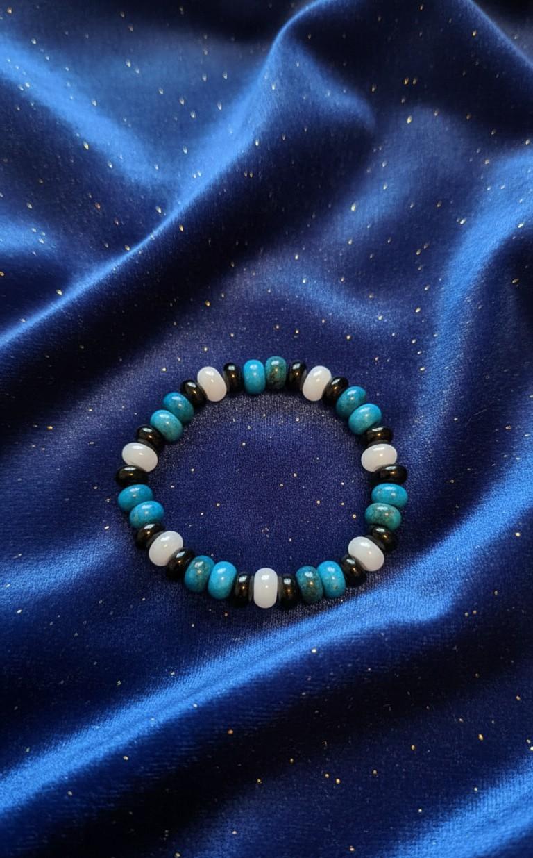 Handgemaakte armband van ronde turquoise, witte en zwarte edelsteenkralen op een glanzende blauwe satijnen ondergrond