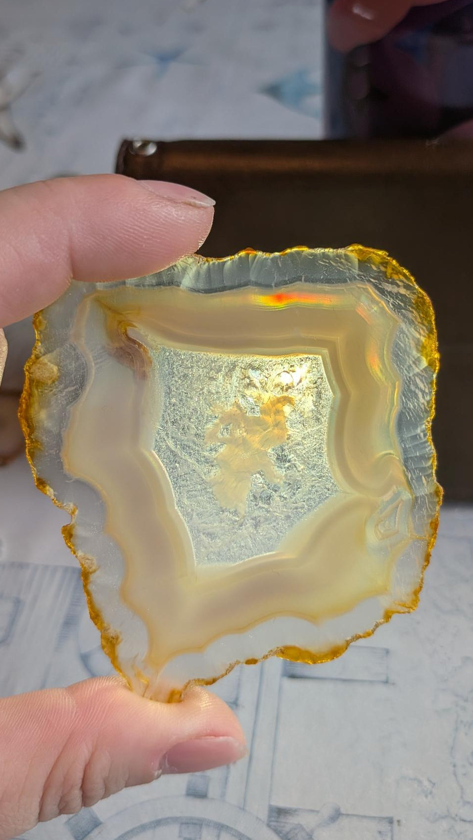 Groot plakje Iris Agaat uit Java (8x7 cm) met een helder centraal venster waarin felle regenboogkleuren zichtbaar zijn door natuurlijke lichtbreking.