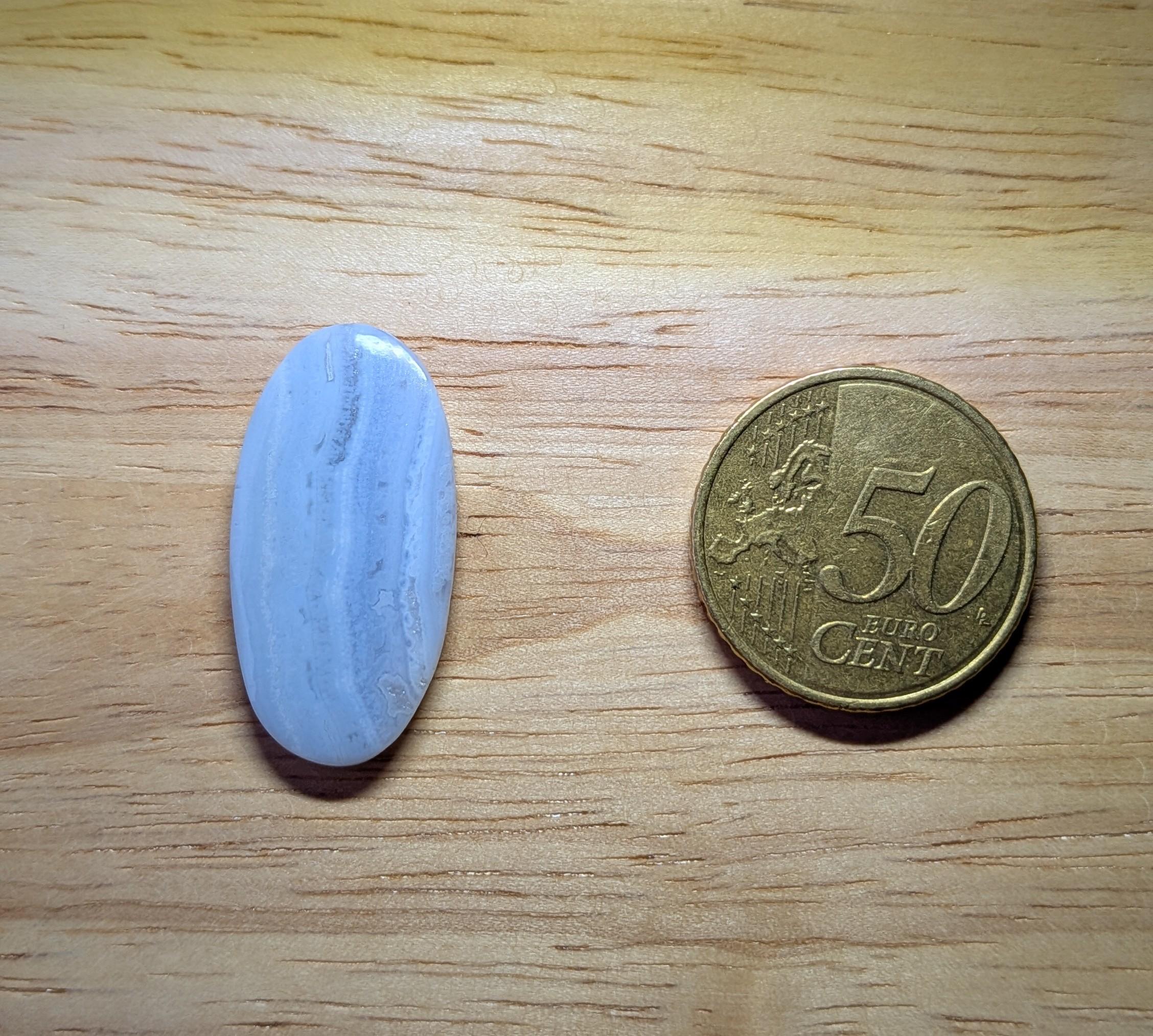 Ovaal geslepen Kantagaat edelsteen met zachtblauwe en witte kleurbanden naast een 50 eurocent munt.