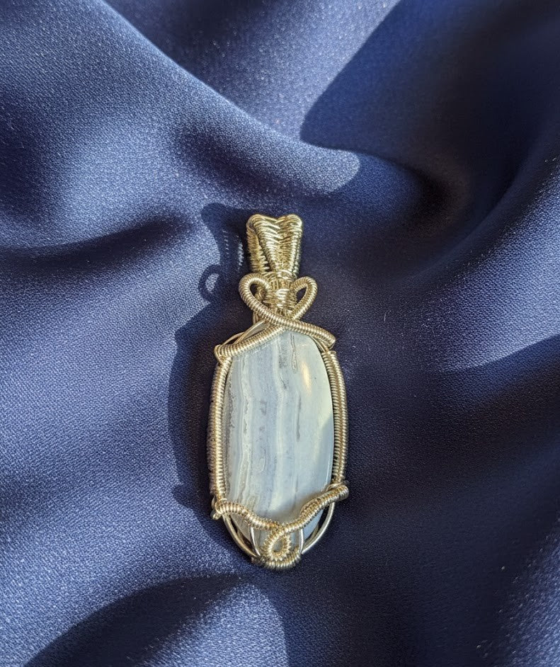 Handgemaakte wire-wrapped hanger van Blauwe Kantagaat met verzilverd draad en een hartvormig detail, gepresenteerd op een diepblauwe glanzende stof.