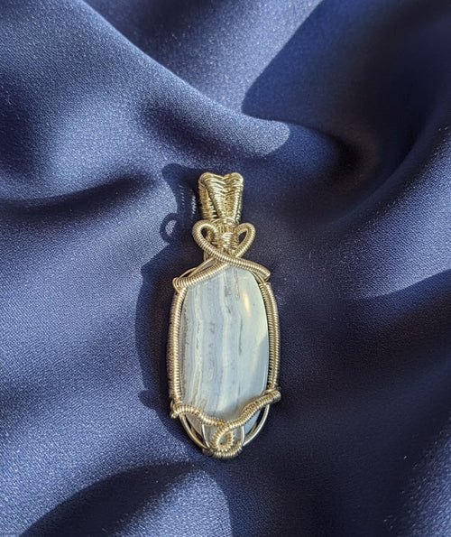 Handgemaakte wire-wrapped hanger van Blauwe Kantagaat met verzilverd draad en een hartvormig detail, gepresenteerd op een diepblauwe glanzende stof.