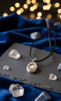 Handgemaakte zilverkleurige wire-wrap hanger met een Labradoriet edelsteen die een gele gloed afgeeft, liggend op een donkere leistenen ondergrond met blauw fluweel en sfeervolle lichtjes op de achtergrond.