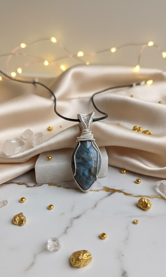 Handgemaakte verzilverde wire-wrap hanger met een blauw-glanzende Labradoriet edelsteen, gepresenteerd op een luxe witte marmeren ondergrond met goudkleurige accenten, champagnekleurige zijde en sfeervolle lichtjes.