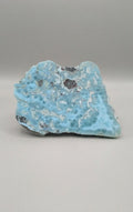 Grote, oceaanblauwe Larimar plak met wolkachtige patronen op een plastic standaard, formaat 11x8 cm.