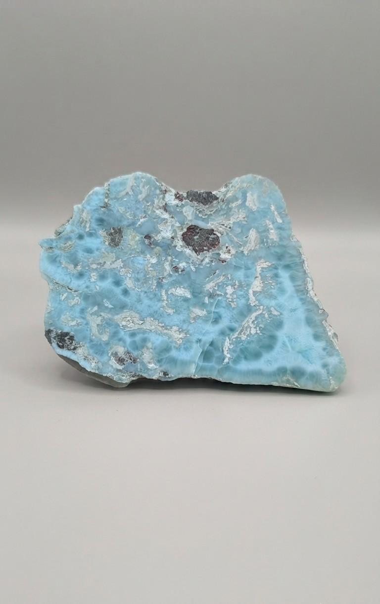 Grote, oceaanblauwe Larimar plak met wolkachtige patronen op een plastic standaard, formaat 11x8 cm.