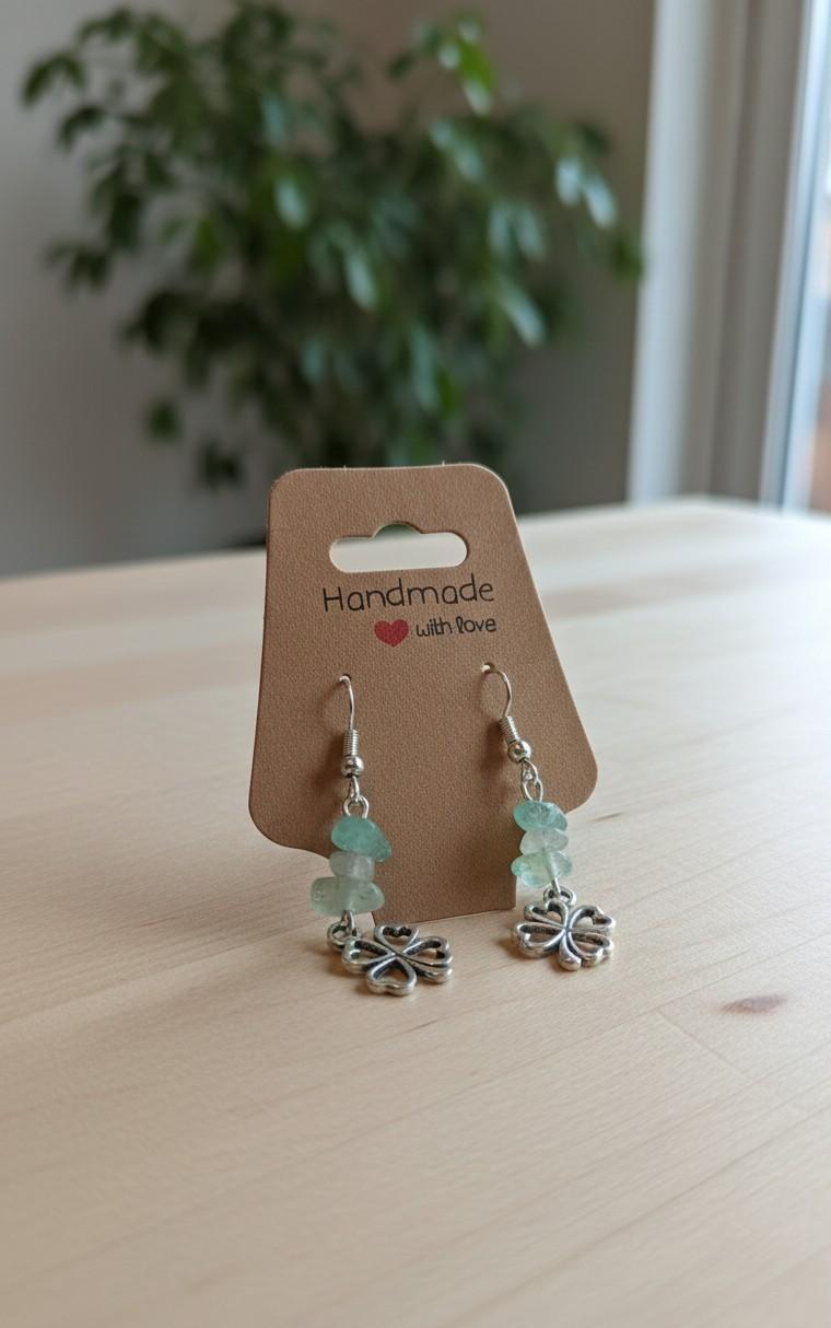 Handgemaakte zilverkleurige oorbellen met klavertje vier bedeltjes en lichtgroene edelsteen splitkralen op een "Handmade with love" kaartje.