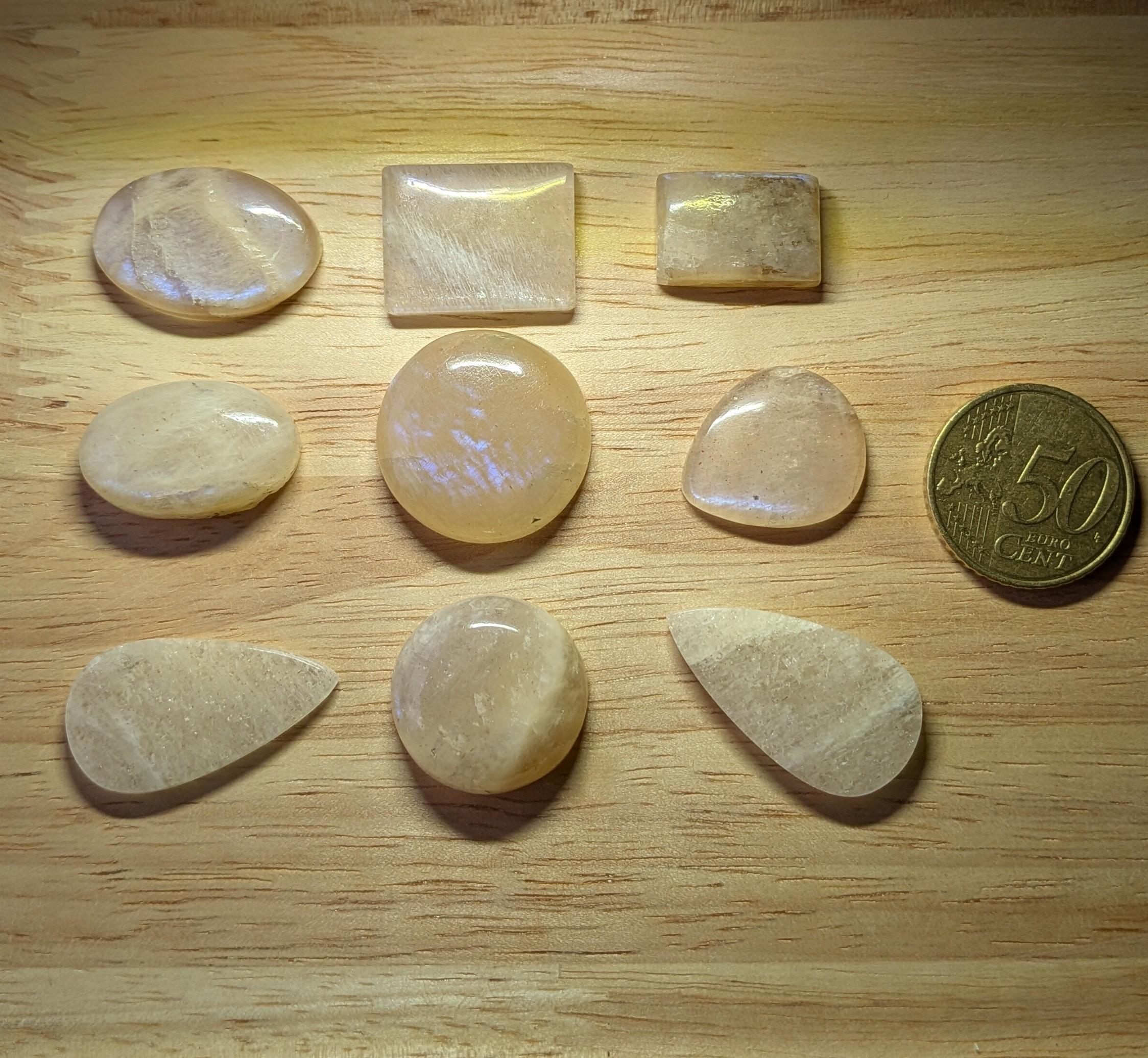 Selectie van perzik en crème Maansteen edelstenen in vormen zoals ovaal, rechthoek en druppel naast een 50 eurocent munt.