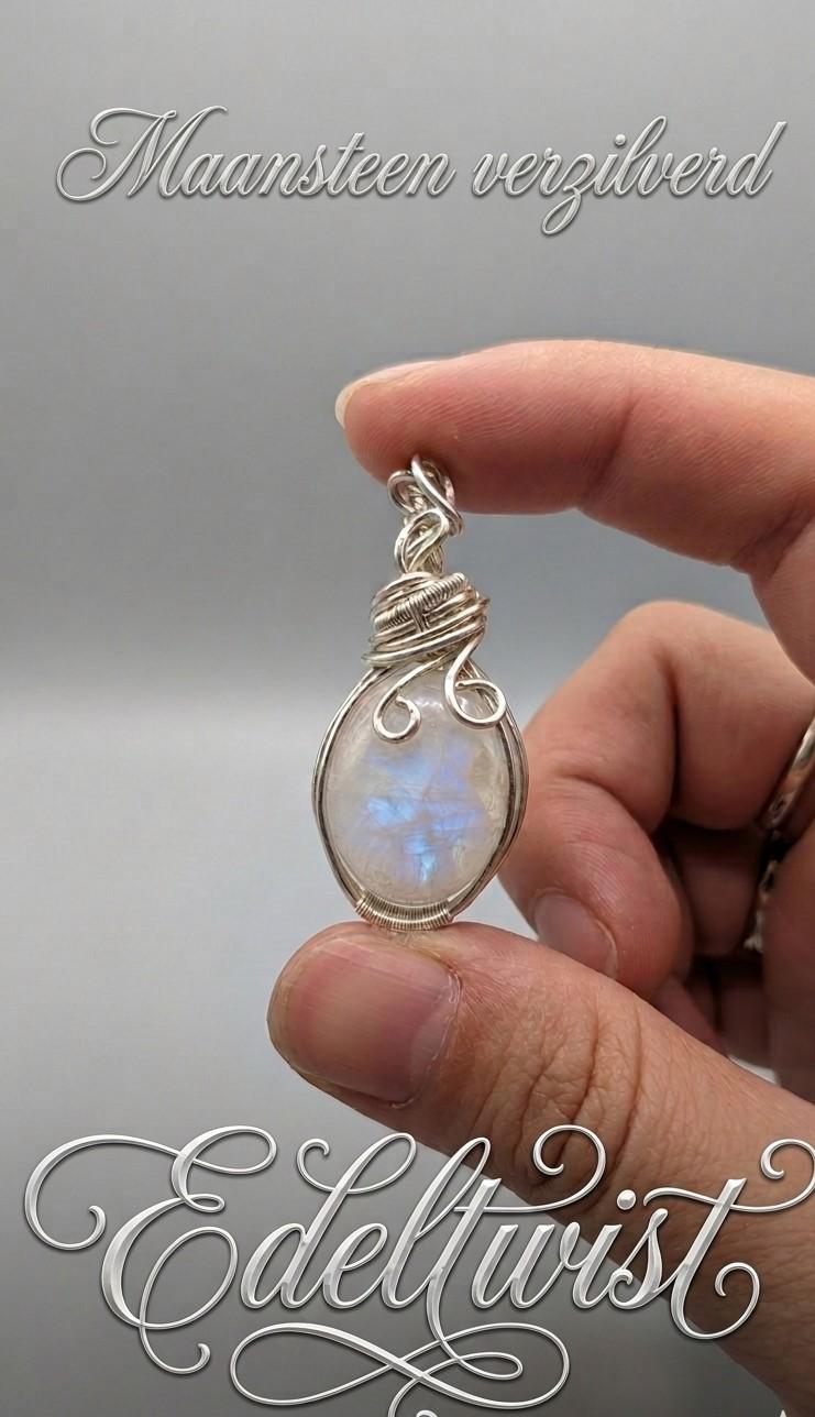 Handgemaakte wire wrapped hanger van Edeltwist met een ovale Regenboog Maansteen die een sterke blauwe flits toont, met de hand gewikkeld in sierlijk verzilverd draad tegen een neutrale, grijze studio-achtergrond.