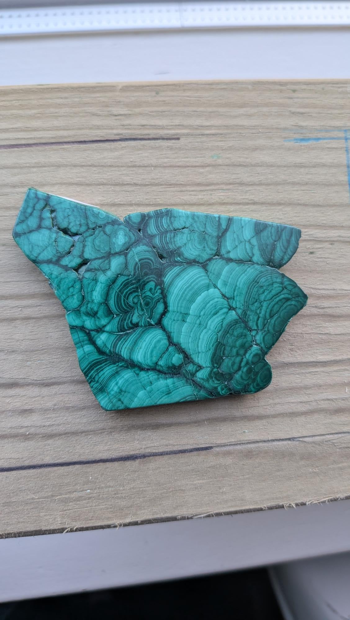 Gepolijst stuk malachiet met diepgroene patronen in de vorm van een wolvenkop, afmeting 7 bij 6.5 cm.