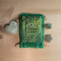 Geschenkset in groen organza zakje met wierook kegels, een pistache calciet hart, een groene aventurijn trommelsteen en een mosagaat ster op een houten achtergrond.