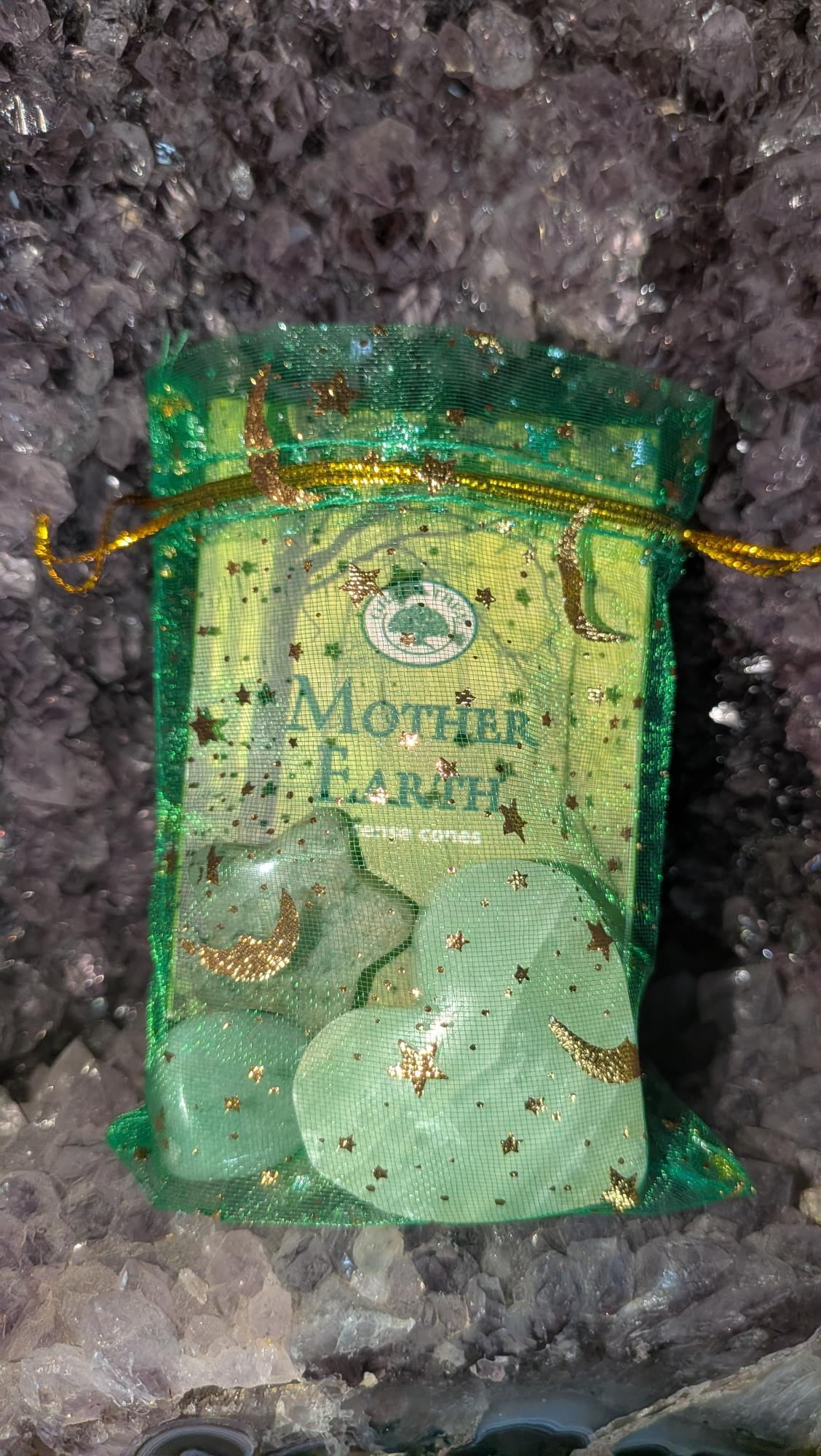 Geschenkset in groen organza zakje met wierook kegels, een pistache calciet hart, een groene aventurijn trommelsteen en een mosagaat ster op een houten achtergrond.