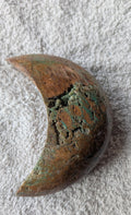 Handgeslepen Oceaan Jaspis halve maan van 242 gram met een uniek patroon van aardse bruintinten en groene ronde orbicles, verticaal gefotografeerd op een witte textiele ondergrond.