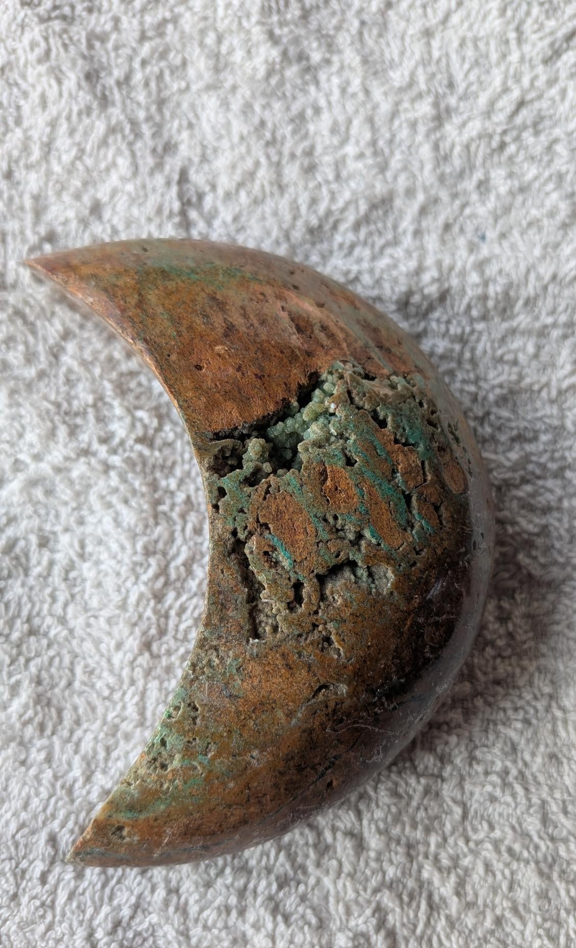 Handgeslepen Oceaan Jaspis halve maan van 242 gram met een uniek patroon van aardse bruintinten en groene ronde orbicles, verticaal gefotografeerd op een witte textiele ondergrond.