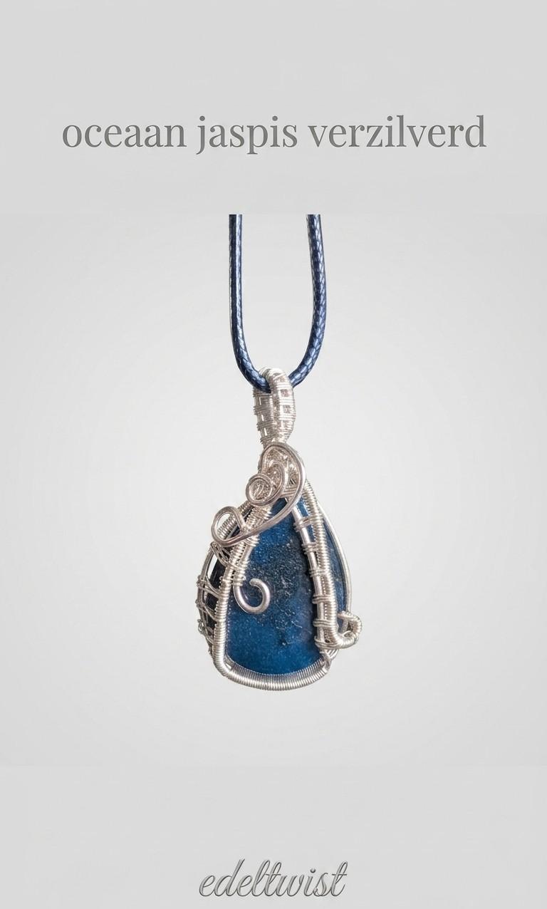 Handgemaakte druppelvormige blauwe Oceaan Jaspis hanger, vakkundig gewrapt in sierlijk verzilverd draad door Edeltwist op een neutrale, lichtgrijze achtergrond.