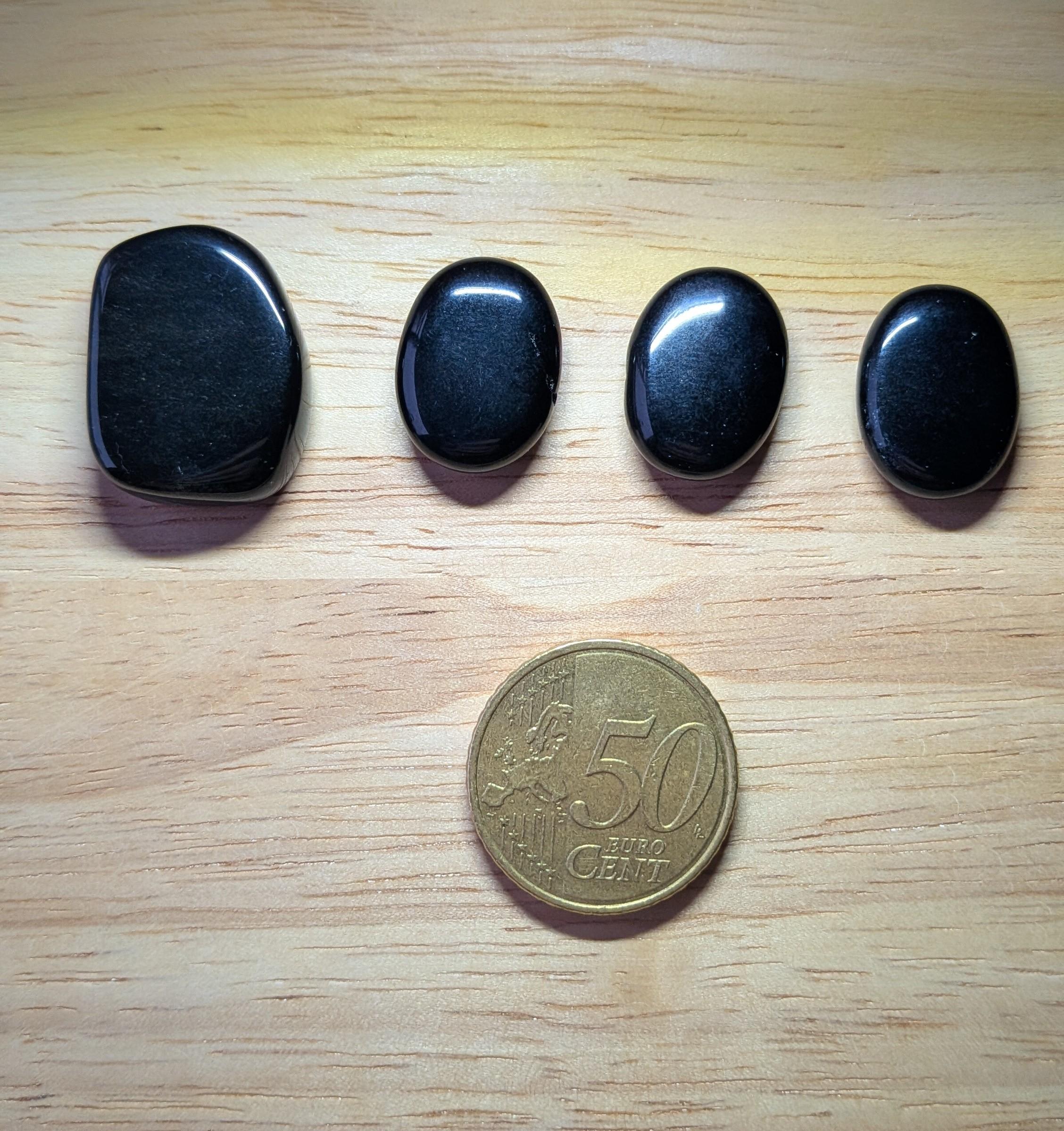 Vier diepzwarte, gladgepolijste Onyx edelstenen in verschillende maten naast een 50 eurocent munt.