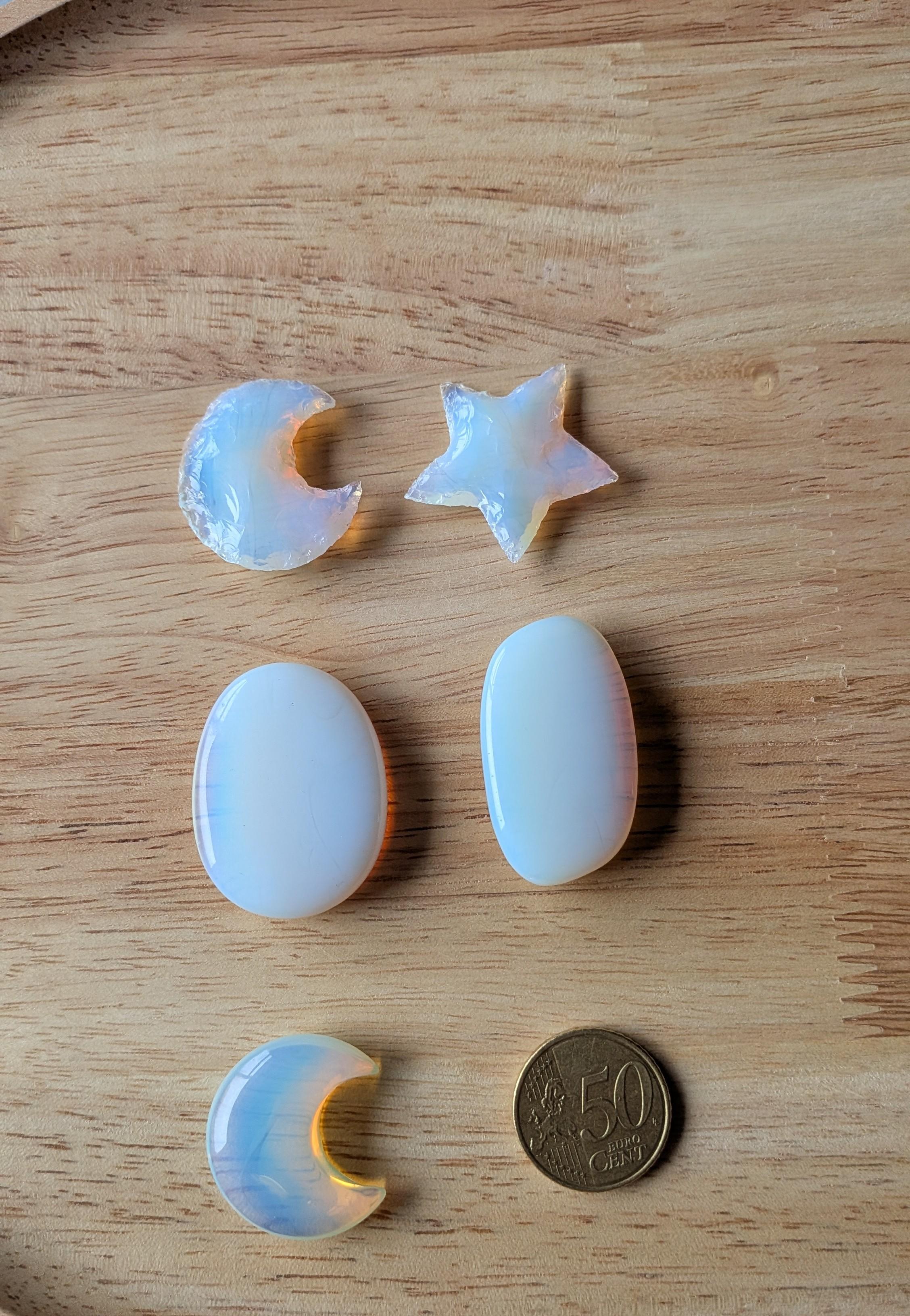 Verschillende vormen gepolijste opaliet, waaronder twee manen, een ster en twee ovalen, naast een 50 eurocent munt op een houten achtergrond.