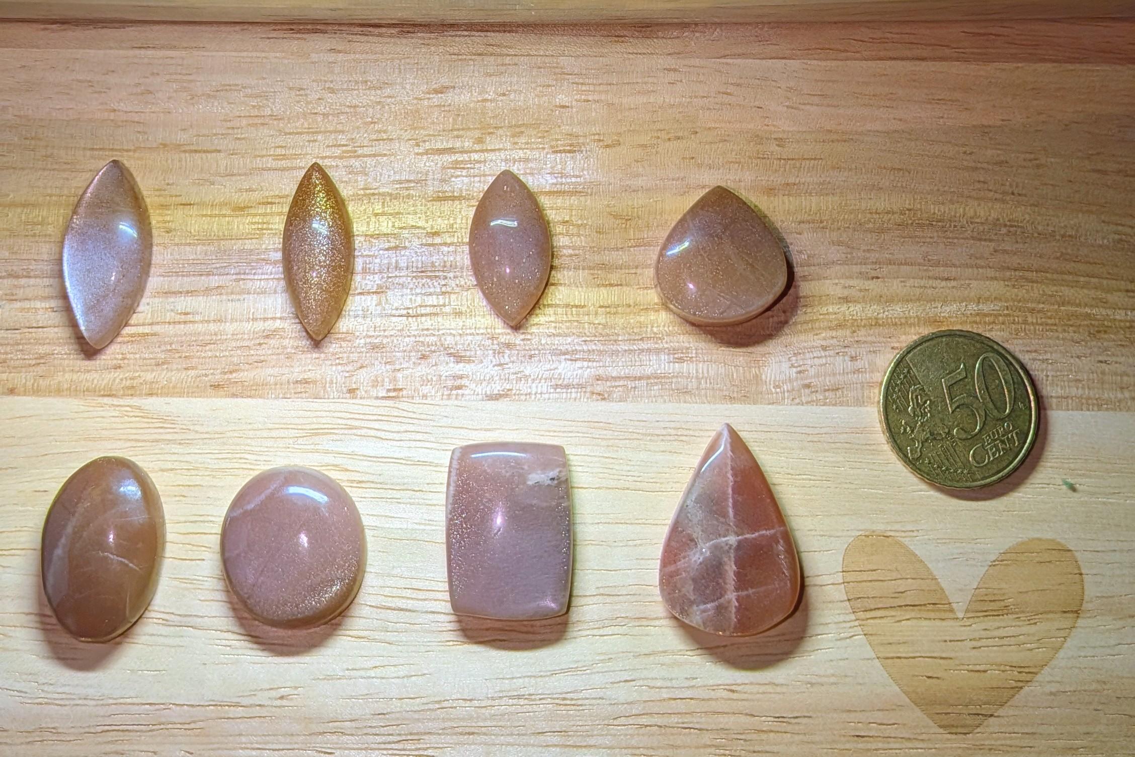 "Collectie Perzik Maansteen edelstenen in marquise, druppel en rechthoek vormen voor handgemaakte wire wrap hangers naast een 50 cent munt."