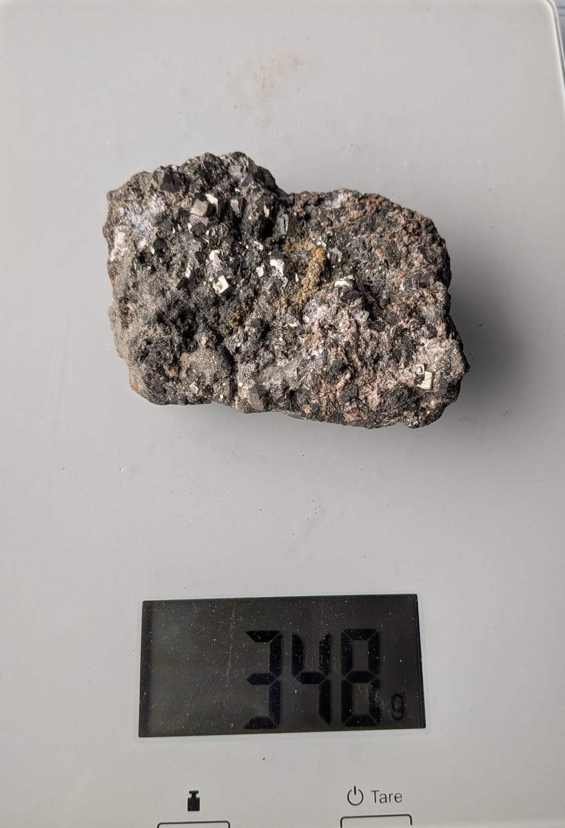 Een ruw, goudkleurig metallic Pyriet cluster van 348 gram met zichtbare kubusvormige kristallen, gefotografeerd op een digitale weegschaal.