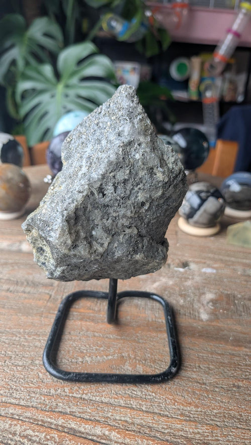 Ruwe grijze steen met goudkleurige pyriet glinsteringen en kwarts op een zwarte metalen standaard, item 215, 527 gram.