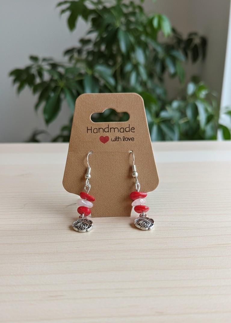 Handgemaakte zilverkleurige oorbellen met een roos bedeltje en rode en roze edelsteen splitkralen op een "Handmade with love" kaartje.