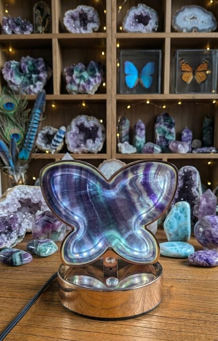 Lichtgevende vlinderlamp gemaakt van paars en groen fluoriet kristal op een houten tafel.