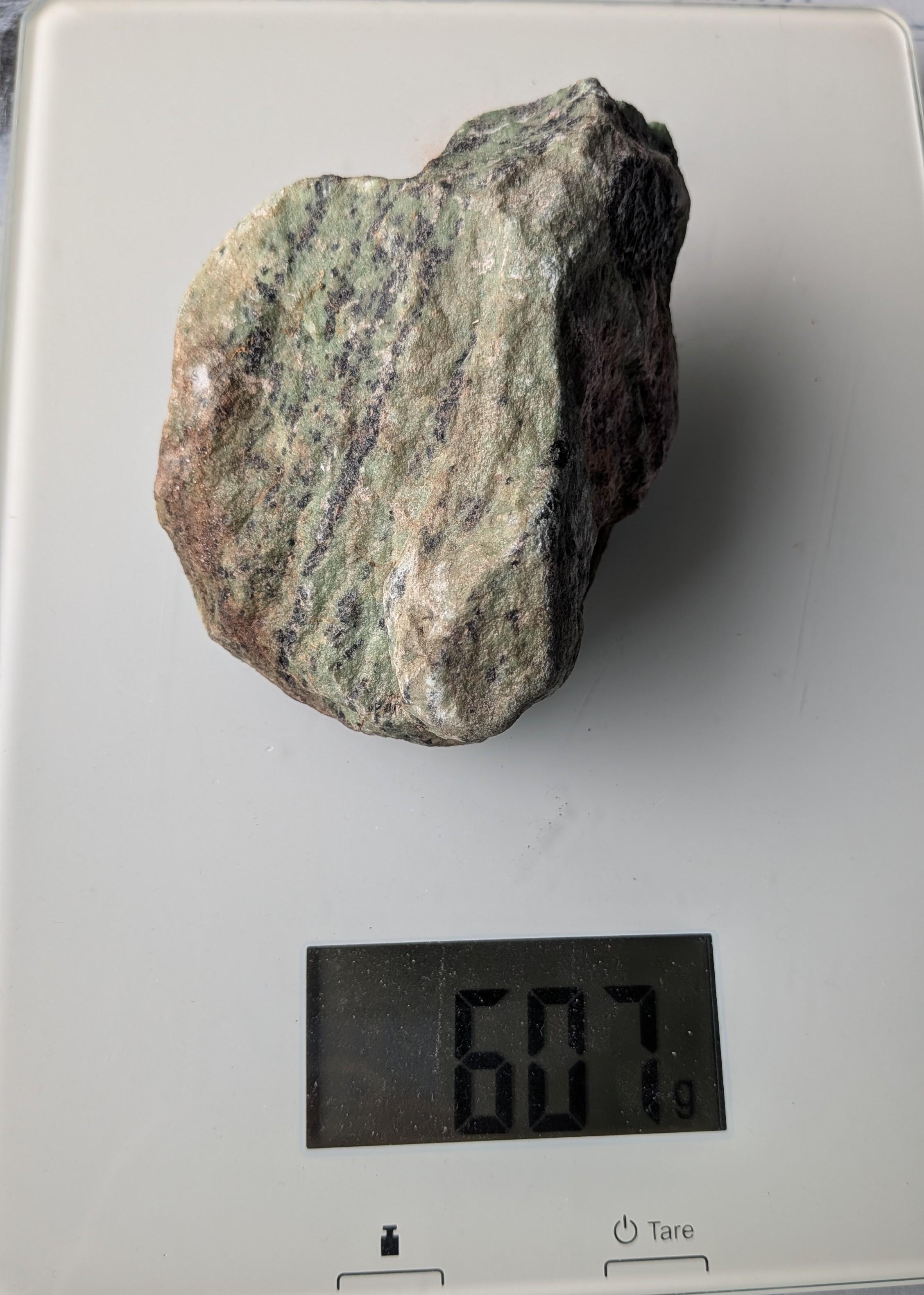 Een robuust, onbewerkt blok Robijn in Zoisiet van 607 gram, met opvallende roze robijn-insluitingen in een groen-zwart gestructureerd zoisiet-gesteente, gefotografeerd op een digitale weegschaal.