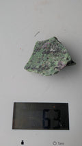 Een ruw stuk Robijn in Zoisiet van 63 gram met levendige groene en rood-paarse tinten, gefotografeerd op een digitale weegschaal.